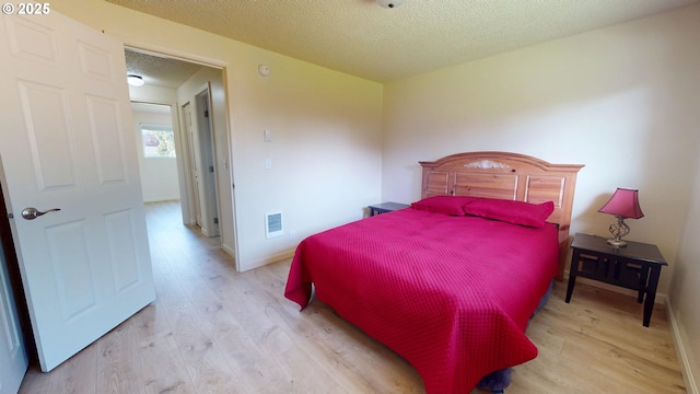 bedroom featuring visible vents, a textured ceiling, light wood finished floors, and baseboards