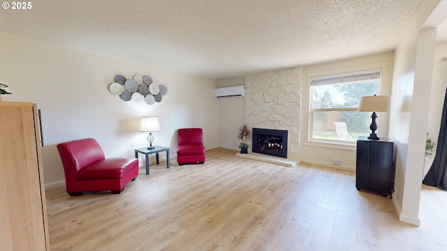 living area with a wall unit AC, a textured ceiling, a stone fireplace, baseboards, and light wood-style flooring