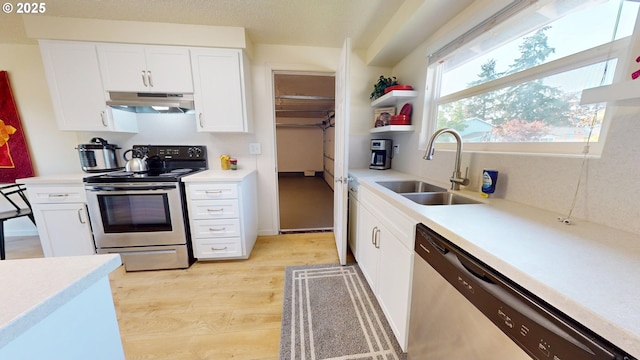 kitchen with white cabinets, a sink, light wood-style flooring, stainless steel appliances, and under cabinet range hood