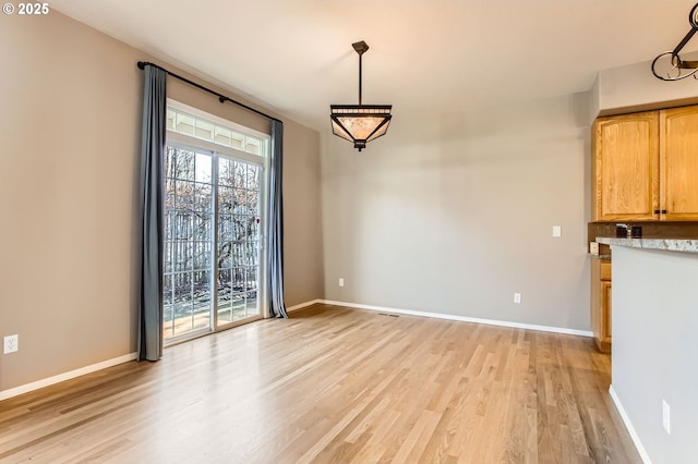 unfurnished dining area with light wood-style flooring and baseboards