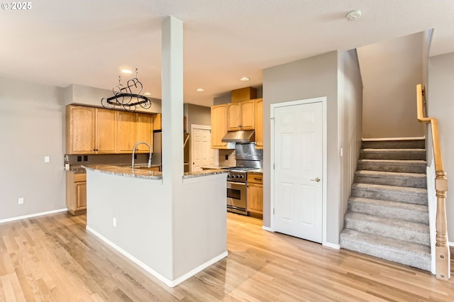 kitchen featuring light wood-style flooring, stainless steel stove, under cabinet range hood, and light stone countertops