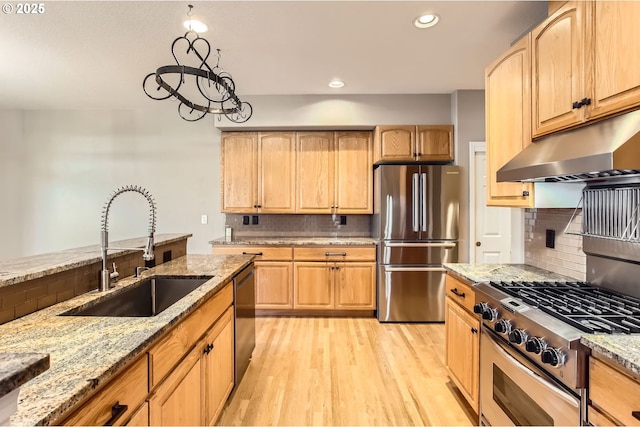 kitchen with light stone countertops, under cabinet range hood, stainless steel appliances, and a sink