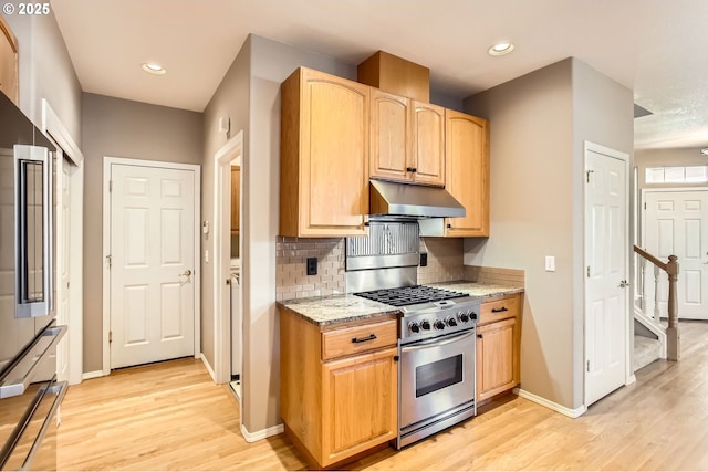 kitchen featuring stainless steel gas stove, tasteful backsplash, light wood-style floors, light stone counters, and under cabinet range hood