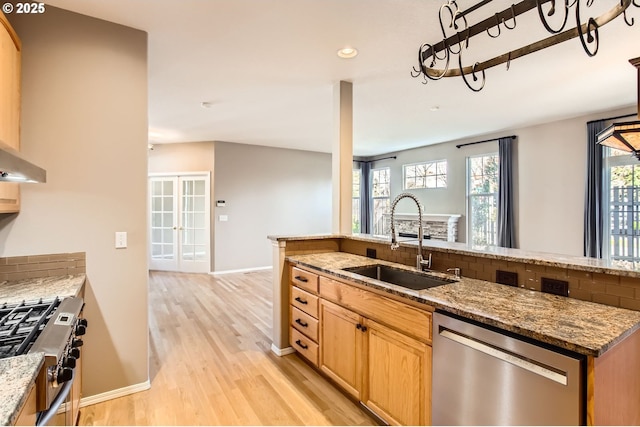 kitchen featuring decorative backsplash, appliances with stainless steel finishes, light wood-style floors, a sink, and light stone countertops