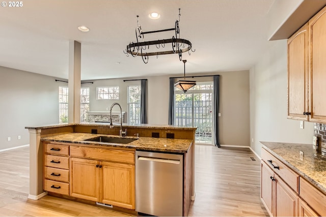 kitchen with light stone counters, stainless steel dishwasher, light brown cabinetry, a sink, and light wood-type flooring