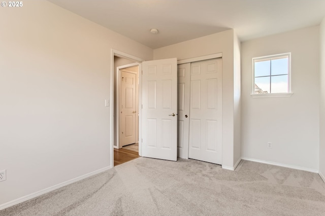 unfurnished bedroom with a closet, light colored carpet, and baseboards