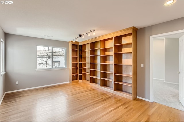 spare room featuring light wood-style floors, baseboards, and rail lighting