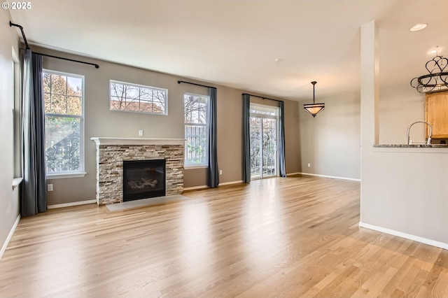 unfurnished living room with light wood-type flooring, a sink, a stone fireplace, and baseboards