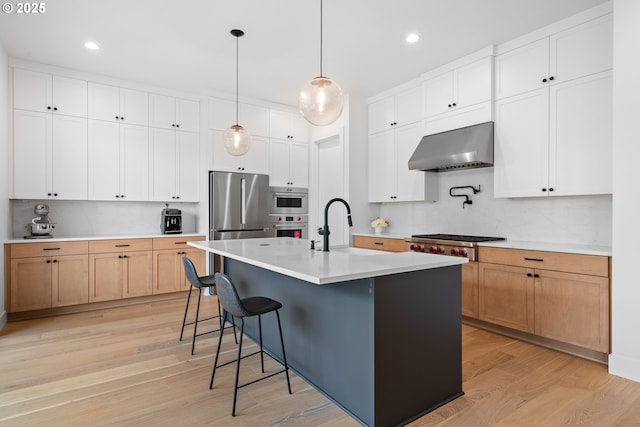 15625 NW Gooderham St, Portland, OR 97229 - kitchen featuring wall chimney exhaust hood, appliances with stainless steel finishes, tasteful backsplash, light wood finished floors, and recessed lighting