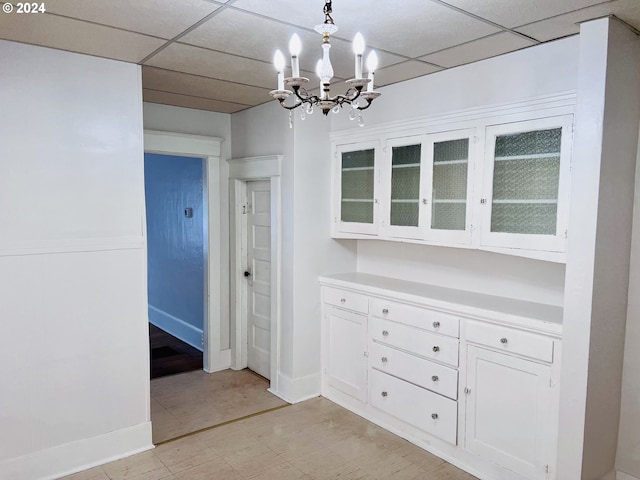 unfurnished dining area featuring a drop ceiling, a notable chandelier, and baseboards