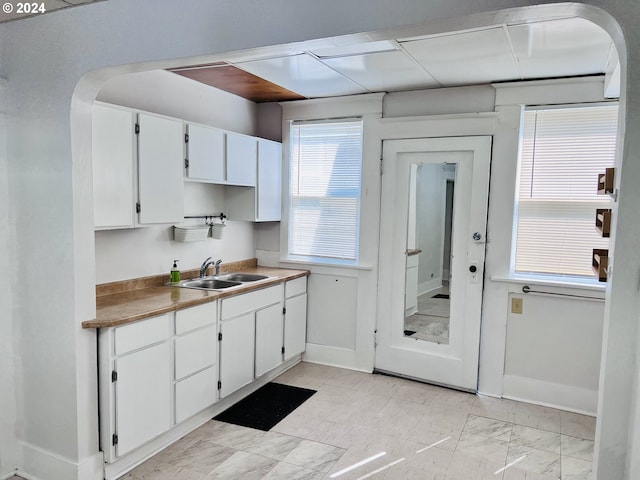 kitchen with marble finish floor, baseboards, white cabinets, and a sink