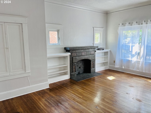 unfurnished living room featuring a textured ceiling, hardwood / wood-style flooring, baseboards, a brick fireplace, and crown molding