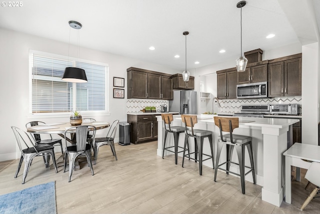 kitchen with a kitchen island with sink, decorative light fixtures, stainless steel appliances, and dark brown cabinetry