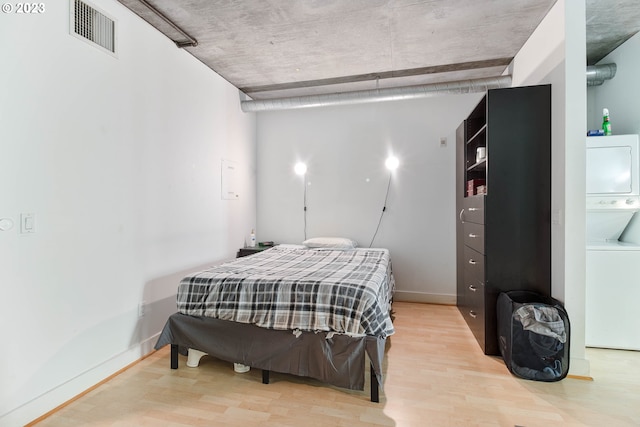 bedroom featuring light hardwood / wood-style floors and stacked washing maching and dryer