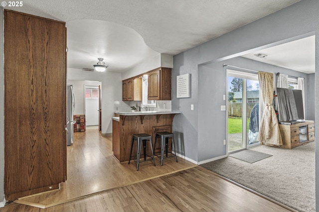 kitchen with a kitchen breakfast bar, brown cabinets, freestanding refrigerator, a peninsula, and light countertops