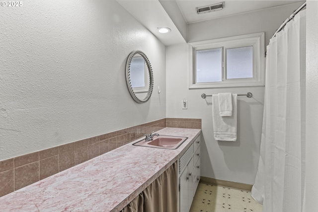 bathroom with a textured wall, vanity, visible vents, and baseboards