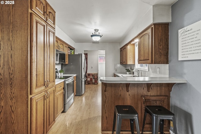 kitchen featuring brown cabinetry, stainless steel appliances, light countertops, and a kitchen breakfast bar