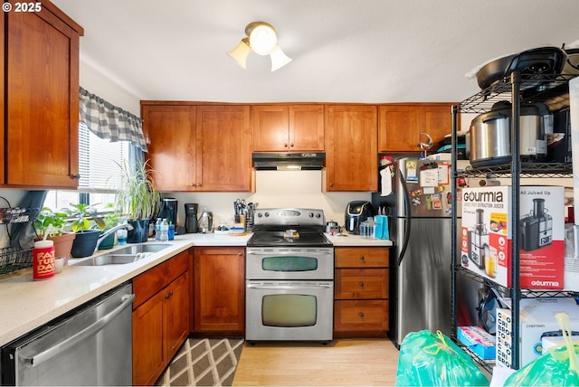 kitchen featuring light wood finished floors, stainless steel appliances, light countertops, a sink, and under cabinet range hood