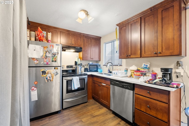 kitchen featuring under cabinet range hood, stainless steel appliances, a sink, light countertops, and dark wood-style floors