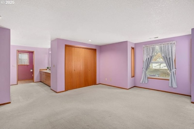 unfurnished bedroom featuring a textured ceiling, light colored carpet, visible vents, baseboards, and a closet