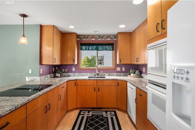 kitchen with a textured ceiling, white appliances, a sink, light wood-style floors, and hanging light fixtures