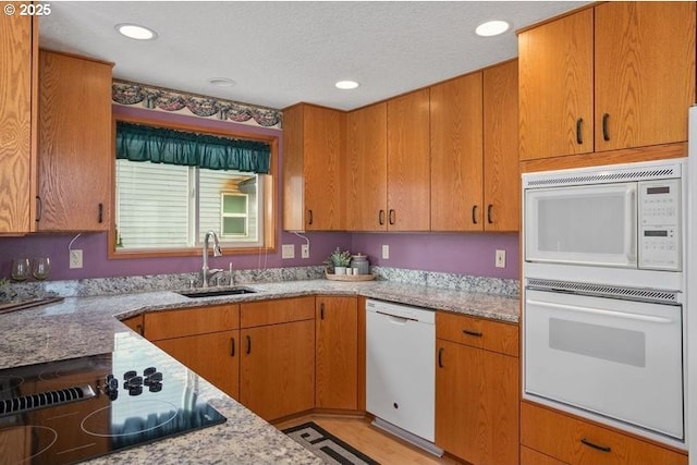 kitchen featuring white appliances, light stone counters, a sink, and recessed lighting