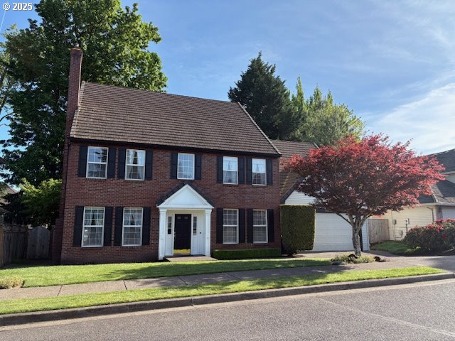 colonial inspired home featuring a chimney, driveway, brick siding, and a garage