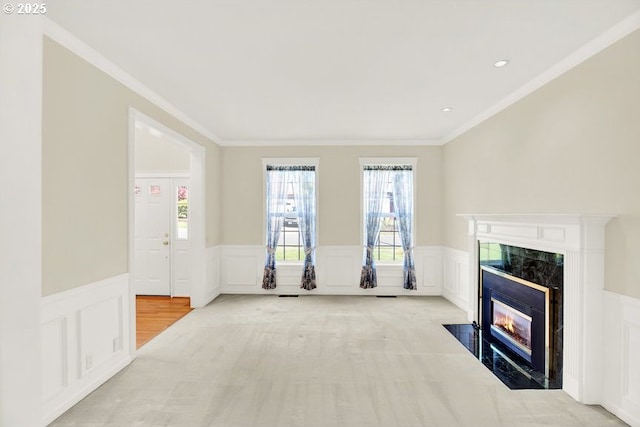 unfurnished living room with a premium fireplace, wainscoting, a decorative wall, and crown molding