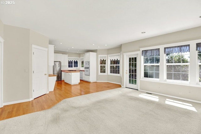 unfurnished living room with baseboards, light colored carpet, recessed lighting, and light wood finished floors