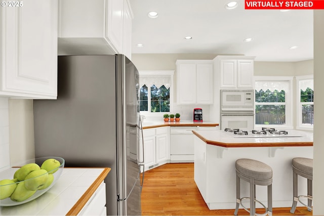 kitchen with white appliances, tile countertops, a kitchen bar, white cabinetry, and recessed lighting