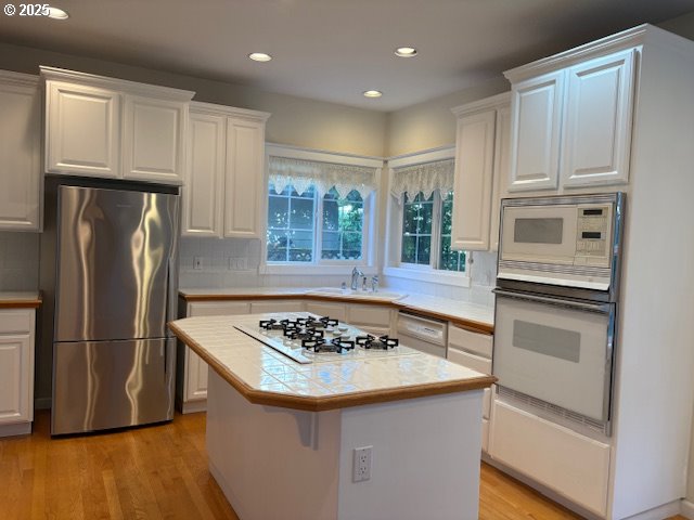 kitchen with white appliances, a sink, white cabinetry, light wood finished floors, and tile countertops