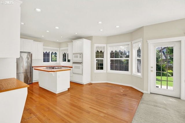 kitchen featuring white appliances, healthy amount of natural light, white cabinets, a center island, and recessed lighting
