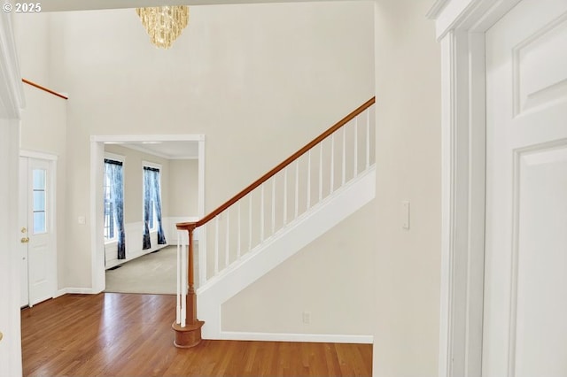 foyer with wood finished floors, stairs, baseboards, a chandelier, and a high ceiling