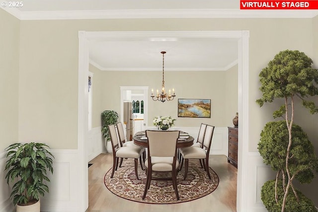 dining room with wood finished floors, crown molding, a chandelier, and wainscoting