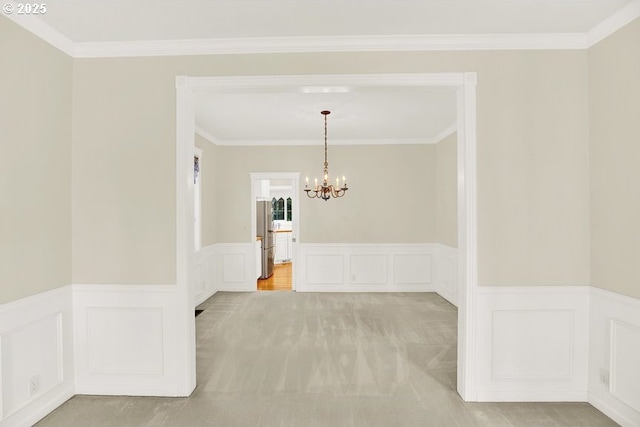 spare room with a chandelier, a decorative wall, a wainscoted wall, crown molding, and light colored carpet