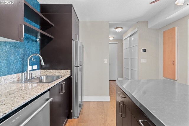 kitchen featuring sink, backsplash, stainless steel appliances, light stone counters, and light wood-type flooring