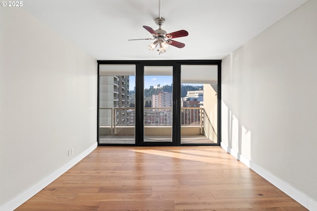 empty room featuring ceiling fan, a wall of windows, and light hardwood / wood-style flooring