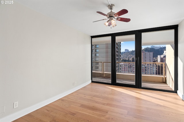 spare room featuring light hardwood / wood-style flooring, ceiling fan, and a wall of windows