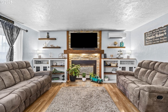 living room with a wall mounted AC, a textured ceiling, a fireplace, and light hardwood / wood-style floors