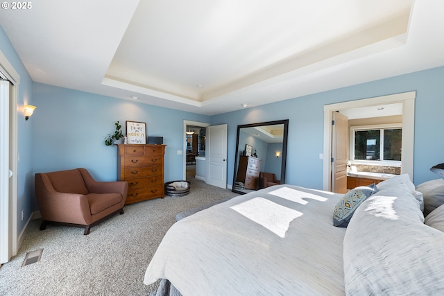 bedroom with carpet flooring, a tray ceiling, and ensuite bath