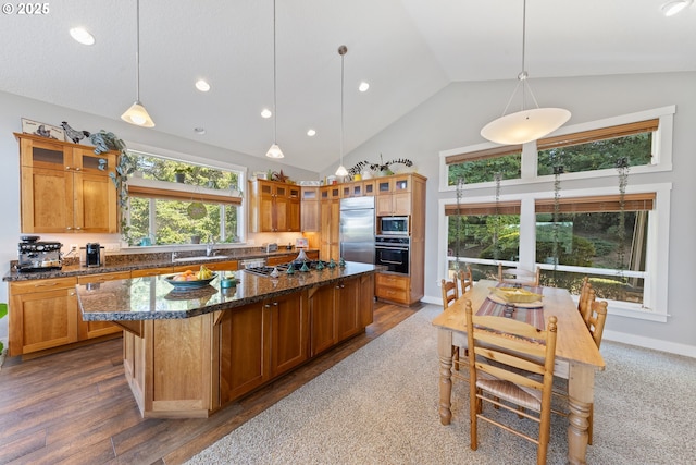 kitchen featuring pendant lighting, a center island, built in appliances, dark stone countertops, and a breakfast bar area