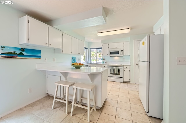 kitchen featuring white appliances, a peninsula, light countertops, white cabinetry, and light tile patterned flooring