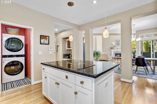 kitchen featuring stacked washer / dryer, black electric stovetop, light wood finished floors, white cabinets, and baseboards