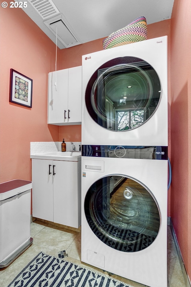 laundry area featuring stacked washer and clothes dryer, cabinet space, and attic access