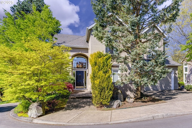 view of front of property featuring stucco siding, a shingled roof, and driveway