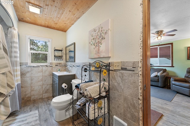 bathroom with tile walls, wood finished floors, a ceiling fan, vanity, and toilet