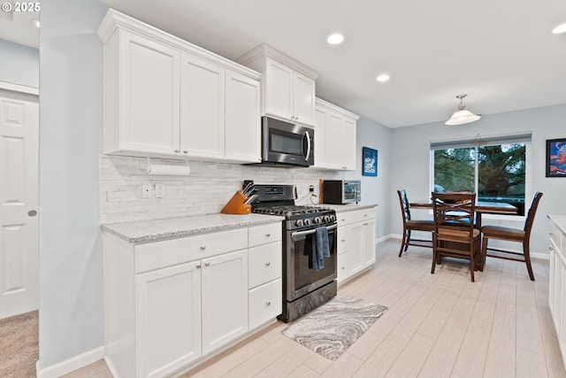 kitchen with tasteful backsplash, light stone countertops, appliances with stainless steel finishes, light wood-type flooring, and white cabinets