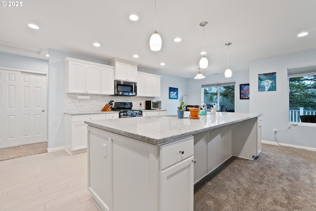 kitchen with white cabinets, light stone countertops, stainless steel appliances, a kitchen island, and backsplash