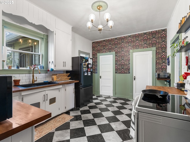 kitchen with sink, black fridge, a notable chandelier, pendant lighting, and white cabinets