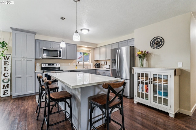 kitchen with appliances with stainless steel finishes, gray cabinets, a breakfast bar area, a center island, and dark wood-style flooring